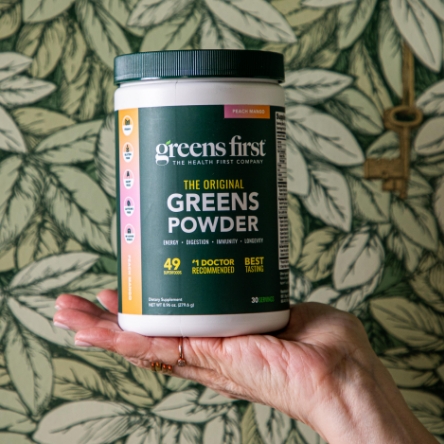 Hand holding a container of Greens First PRO powder