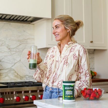 Woman drinking a glass of Greens First powder in the kitchen